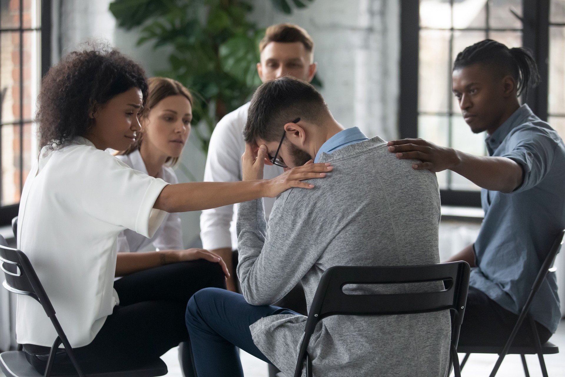 Diverse Menschen unterstützen unglücklichen Mann bei der Therapiesitzung, berührenschulternd.